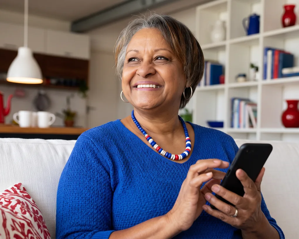 Mulher sorrindo no sofá de casa com o celular na mão